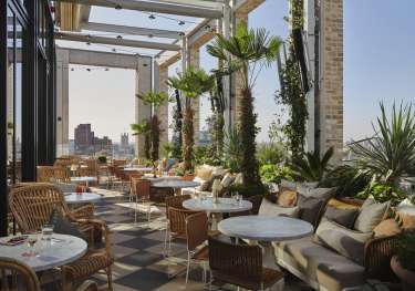 Rooftop bar with round tables, chairs, and plants .