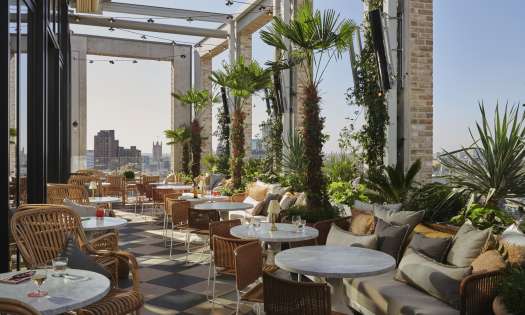 Rooftop bar with round tables, chairs, and plants .