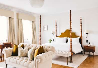 Four-posted bed and cream sofa in hotel bedroom.