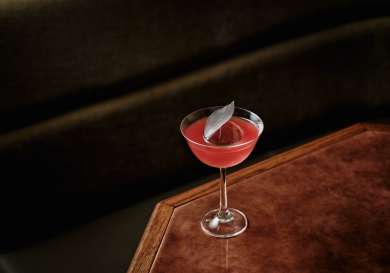 Red cocktail placed on wooden table in bar.