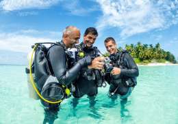 Three divers admiring a photo in the waters of maldives.