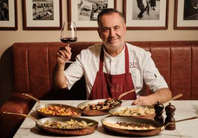 Chef at tozi restaurant with five different dishes and a glass of red wine .