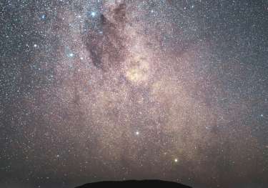 Uluru at night with stars above it.