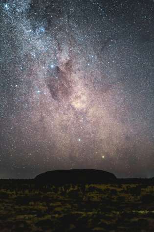Uluru at night with stars above it.