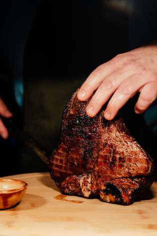 Chef slicing woodfired meat at restaurant .