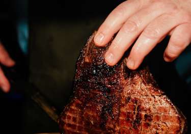 Chef slicing woodfired meat at restaurant .