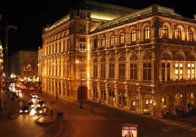 An illuminated, ornate building stands lit at night, with cars driving on a city street nearby.