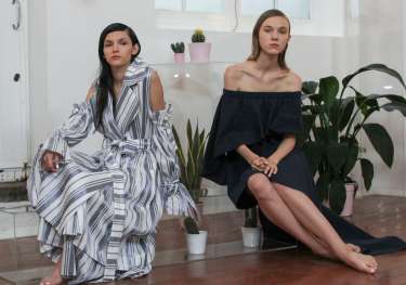 Two women are seated in a minimalist, plant-filled room.