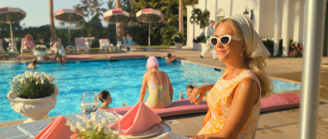 actress sitting beside pool in orange mini dress