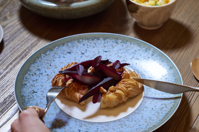 someone cutting into pastry topped with red fruit