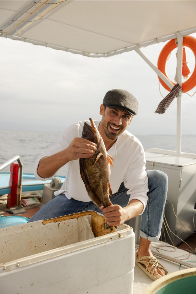 a fisherman in corfu holding a single fish in the air