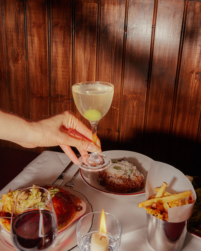 person holding cocktail over table topped with food 