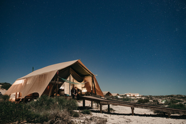 person sitting outside canvas tent during night
