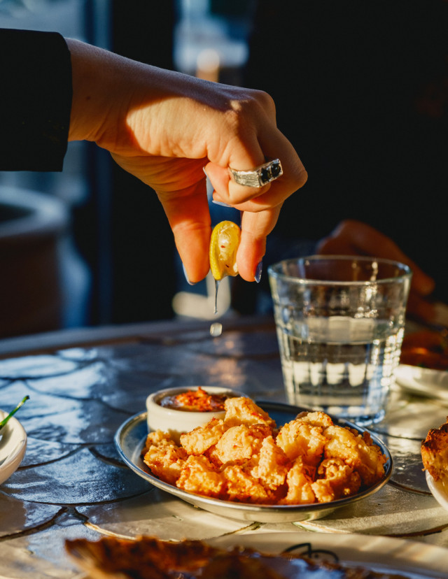 person squeezing lemon wedge onto a plate of crispy calamari