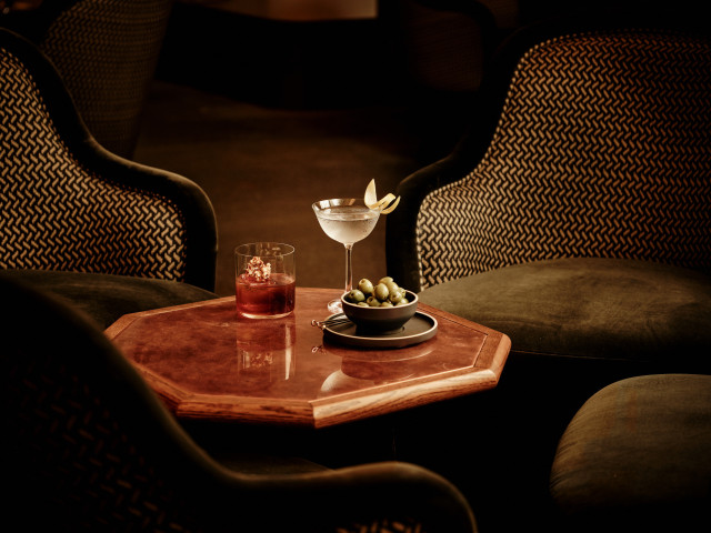 two cocktails served on wooden table with a bowl of olives
