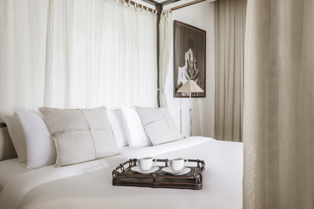 hotel bed with a wicker tray holding two white tea cups