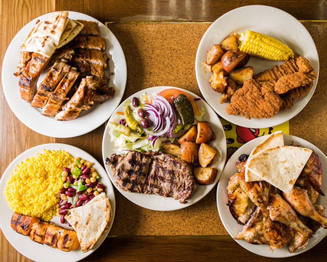 Mix of plates filled with traditional southern food, including corn, steak, friend chicken and rice.