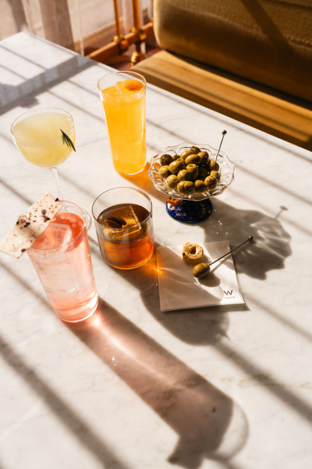 four cocktails on a marble surface with a bowl of green olives